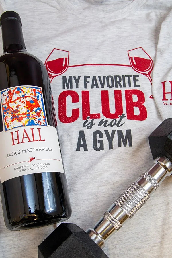 Flat lay image of the HALL "Gym" shirt with a dumbbell and bottle of 2019 HALL Jack's Masterpiece Cabernet Sauvignon.