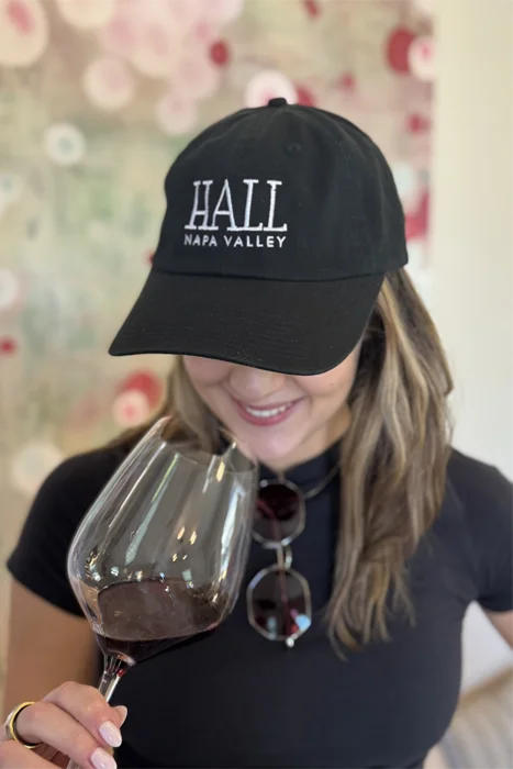 Image of a woman wearing a HALL Baseball Hat holding a glass of red wine